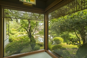 A room with a large window overlooking a lush garden with various plants and a pond. - Ikuji Onsen TANAKAYA (Kurobe)