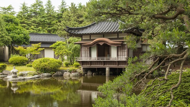 A traditional Japanese building with a wooden balcony, surrounded by lush greenery and a calm pond. - Ikuji Onsen TANAKAYA (Kurobe)