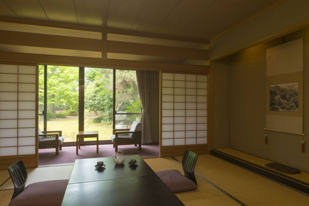 A traditional Japanese room with tatami flooring, a low table with a tea set, and sliding doors leading to a garden.