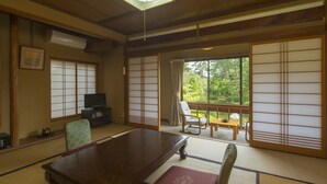 A traditional Japanese room with tatami flooring, a wooden table, a television, and sliding doors leading to a balcony with a view of greenery. - Ikuji Onsen TANAKAYA (Kurobe)