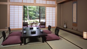 A traditional Japanese room with tatami flooring, a low table with cushions, and sliding doors leading to an outdoor garden. - Ikuji Onsen TANAKAYA (Kurobe)