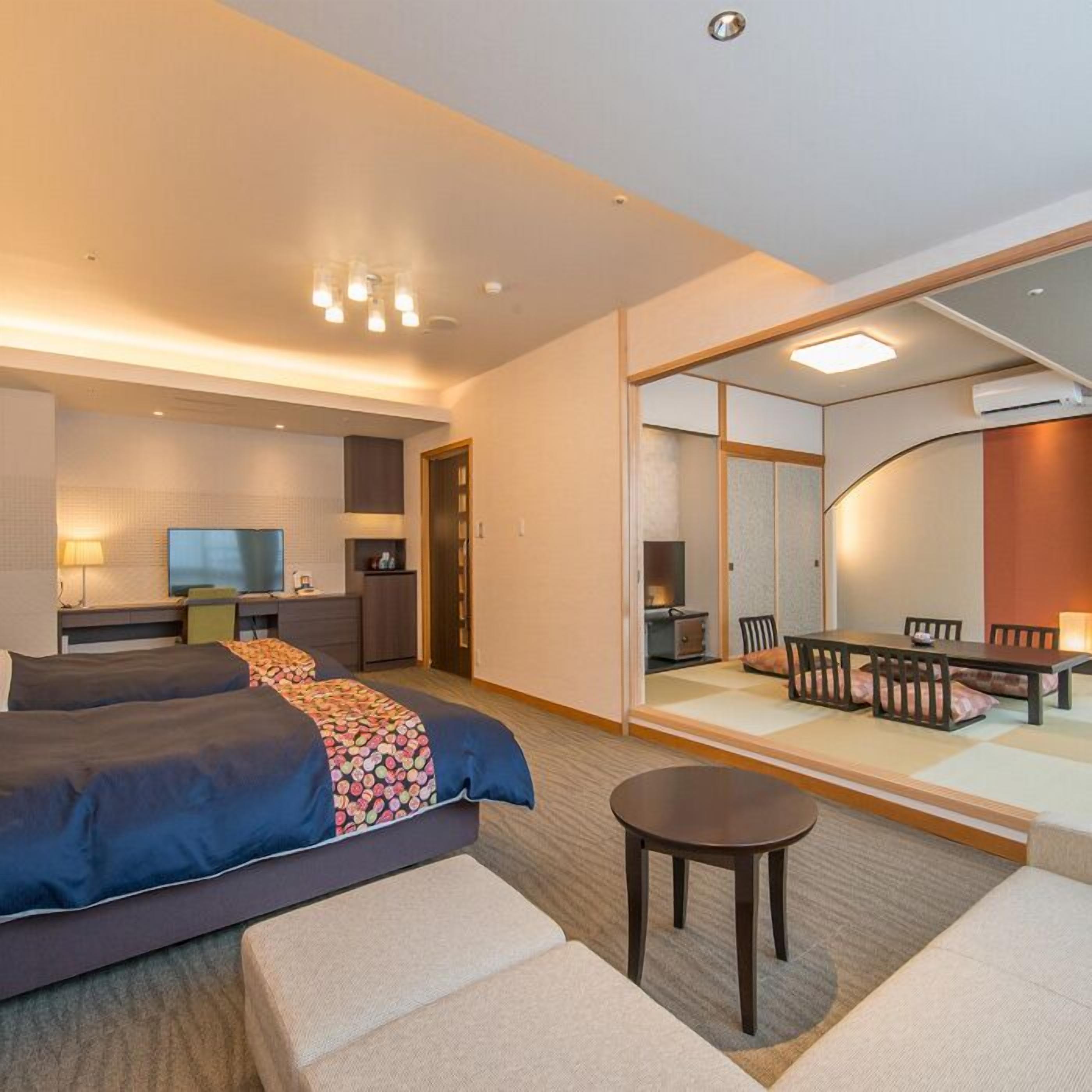 A hotel room with a bed, a desk, a chair, a small table, and a dining area with a table and chairs.
