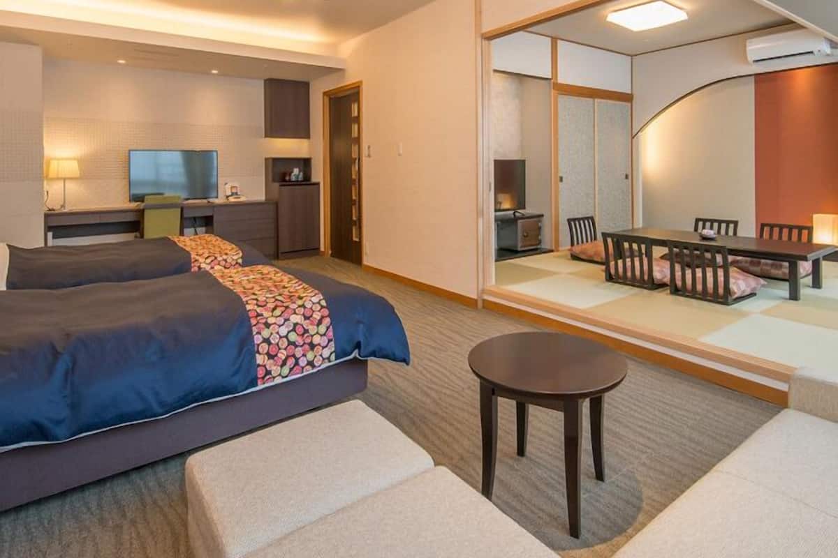 Ett hotellrum med en säng, ett skrivbord, en stol, ett litet bord och en matplats med ett bord och stolar.