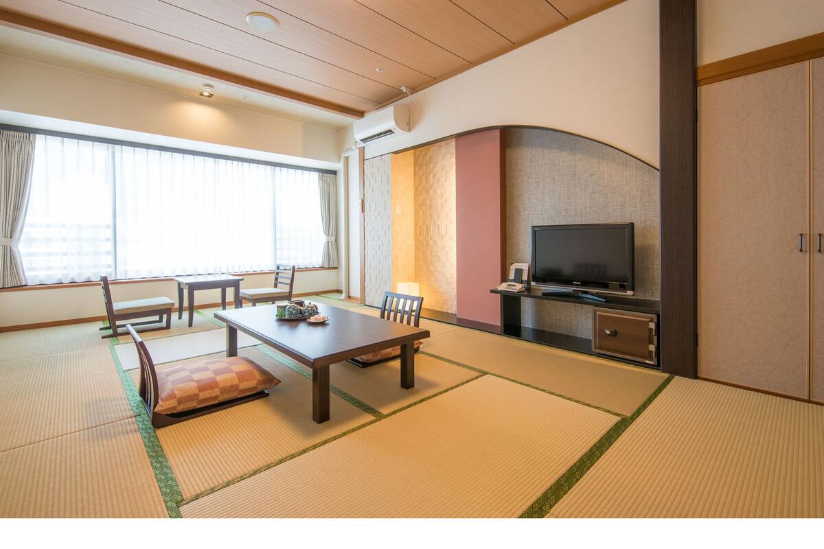 Ett traditionellt japanskt rum med tatamimattor på golvet, ett lågt bord med kuddar, en tv och en skjutdörr.