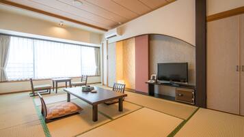 Una habitación tradicional japonesa con suelo de tatami, una mesa baja con cojines, un televisor y una puerta corredera.