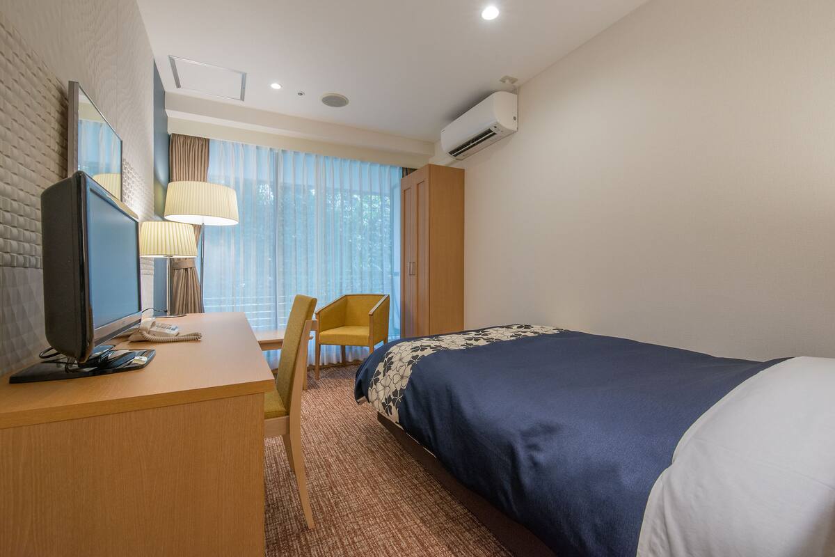 Ett hotellrum med en säng, ett skrivbord, en stol, en tv och en luftkonditioneringsanläggning.