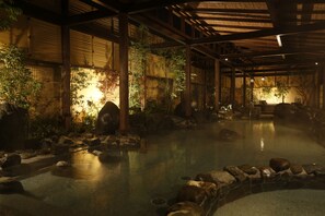 A traditional Japanese onsen with a stone bath surrounded by rocks and bamboo walls. - New Welcity Yugawara (Atami)