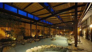 Un onsen japonés tradicional con un balneario de piedra rodeado de rocas, vigas de madera y plantas de bambú.