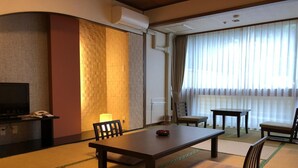Una habitación de estilo japonés tradicional, con suelo de tatami, una mesa baja con sillas, un televisor y una puerta corredera.
