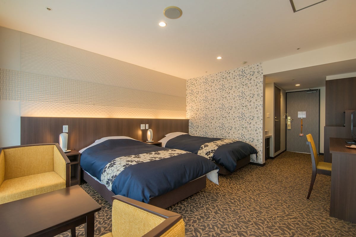 Ett hotellrum med två sängar, ett skrivbord, en stol och en mönstrad matta.