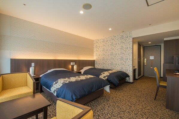 A hotel room with two beds, a desk, a chair, and a patterned carpet.