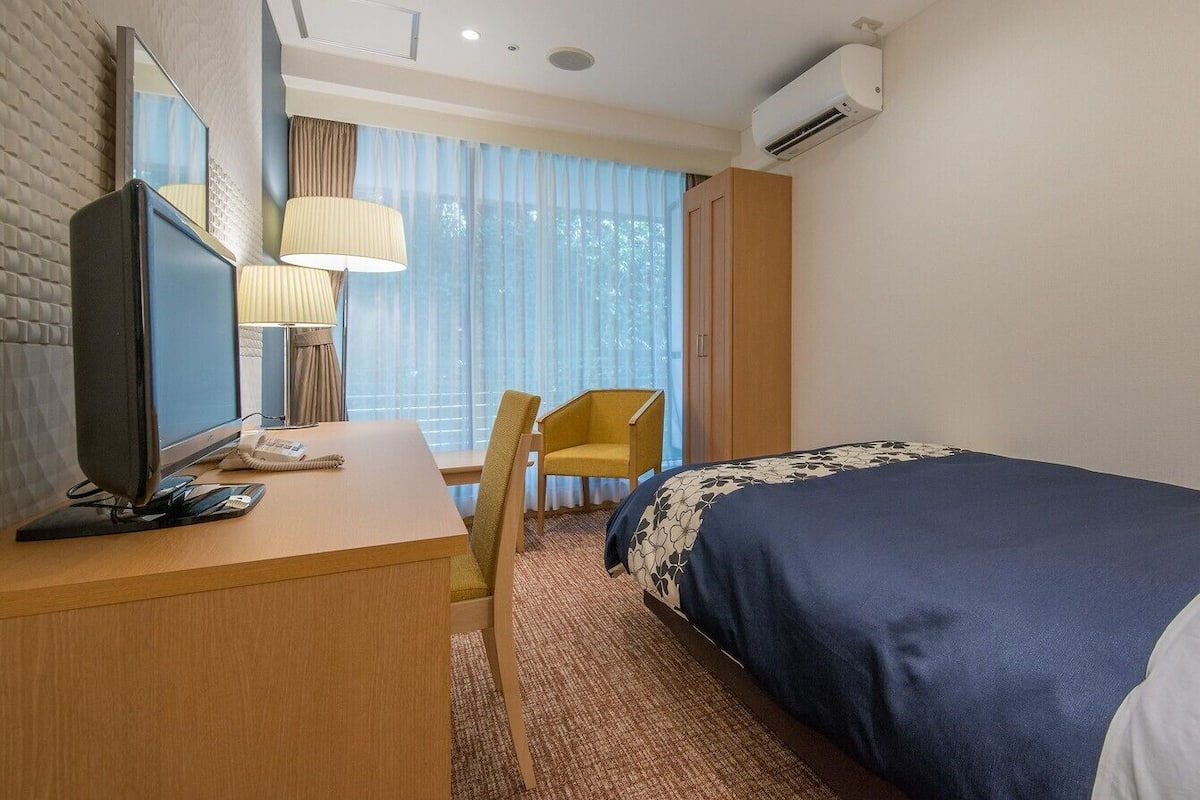 Une chambre d’hôtel équipée d’un lit, d’un bureau avec un ordinateur, d’une chaise, d’un téléviseur et d’un appareil de climatisation.