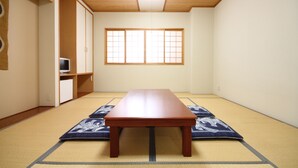 Ein traditioneller japanischer Raum mit Tatami-Boden, einem Holztisch und einem Fernseher auf einem Regal.