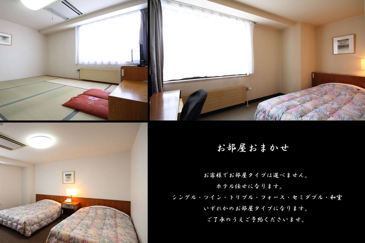 Une chambre d’hôtel avec un sol recouvert de tatamis, un lit avec une couette à motifs floraux, un bureau avec une chaise et une fenêtre avec des rideaux.