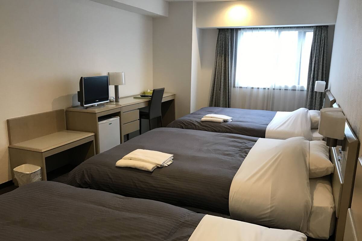 Habitación de hotel con dos camas, un escritorio, una computadora y un ventanal con cortinas.