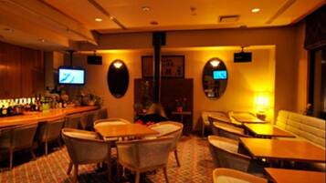 A hotel lobby with a bar area, seating arrangements, and a television screen.