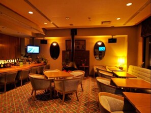Una hall d'albergo con zona bar, posti a sedere e uno schermo televisivo.
