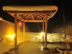 Un'area esterna innevata con una struttura in legno, probabilmente un gazebo, e un pavimento riscaldato.