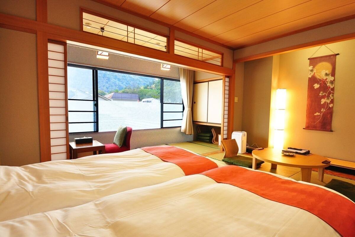 A hotel room with a large bed, a small table, a chair, and a view of the outside.