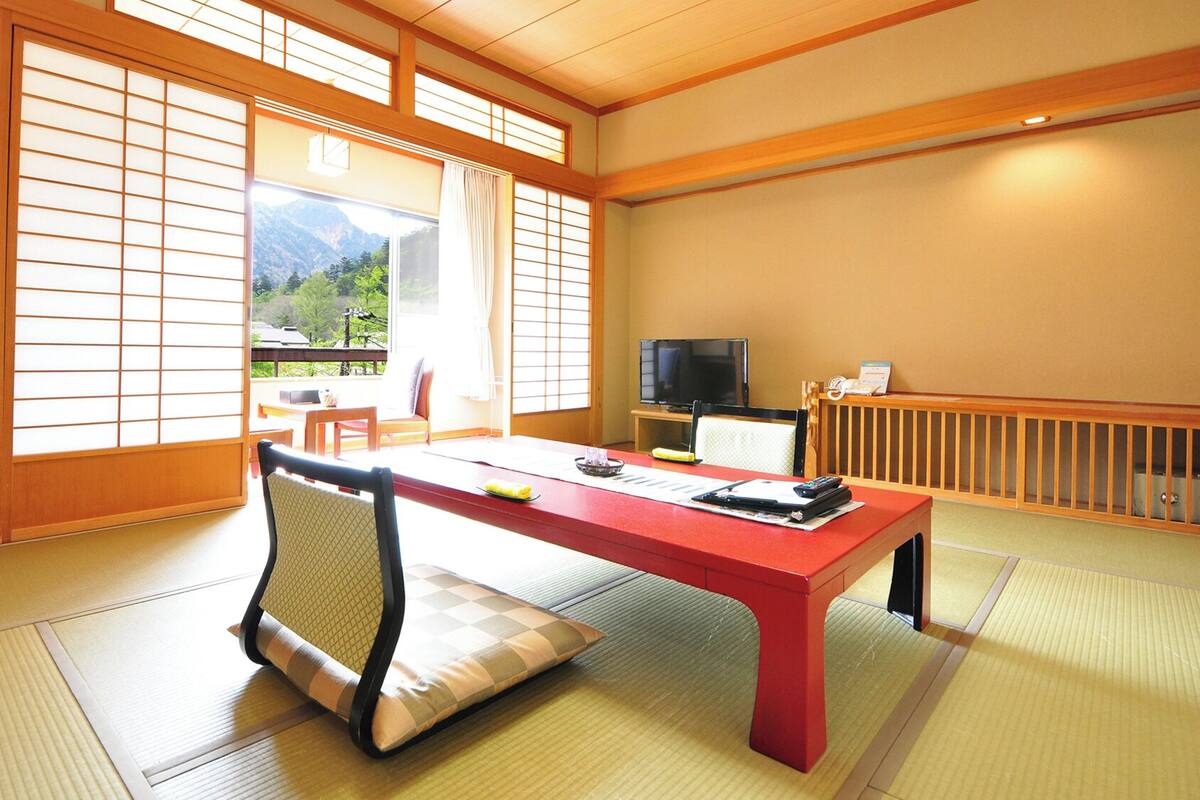 A traditional Japanese room with tatami flooring, a low table, a television, and a view of mountains.