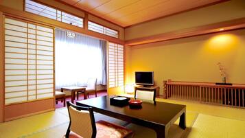 A traditional Japanese room with tatami flooring, a low table, a television, and sliding doors.