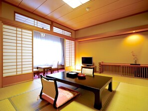 Una tradizionale stanza giapponese con pavimento in tatami, un tavolino, un televisore e porte scorrevoli.