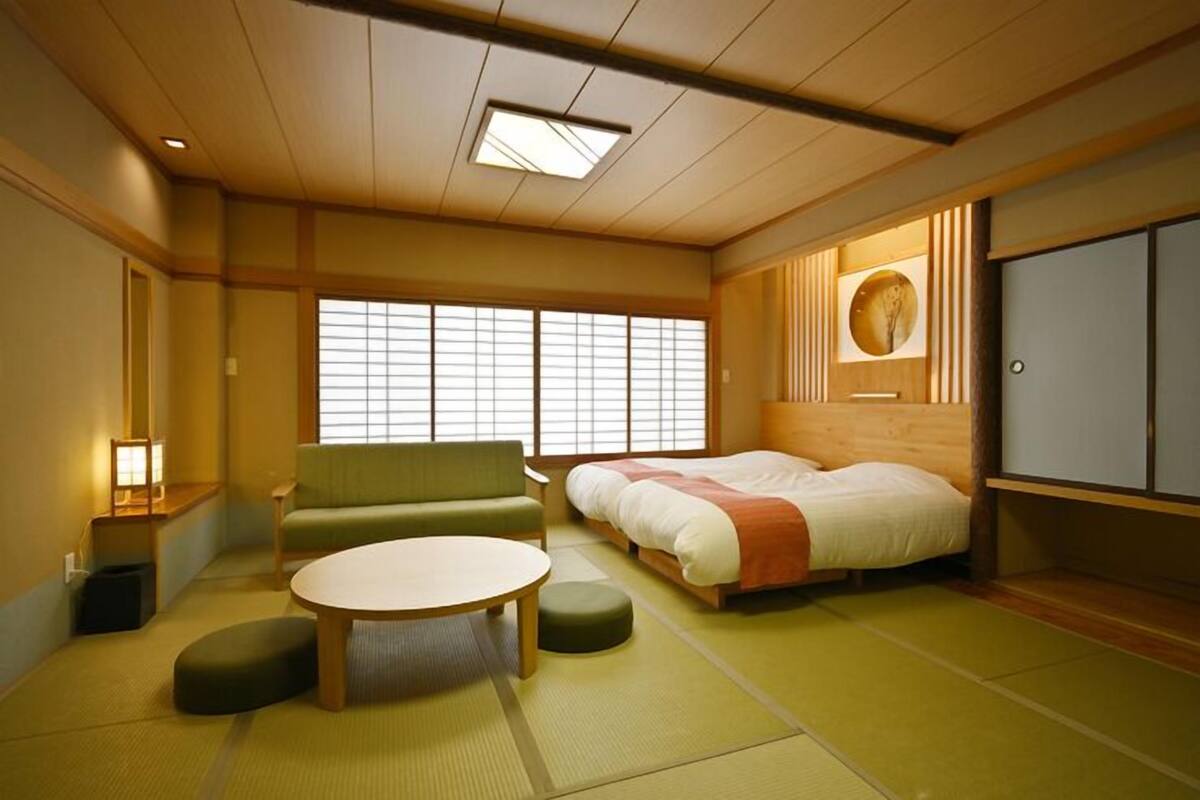A traditional Japanese-style room with tatami flooring, a low wooden bed, a green sofa, and a round table.