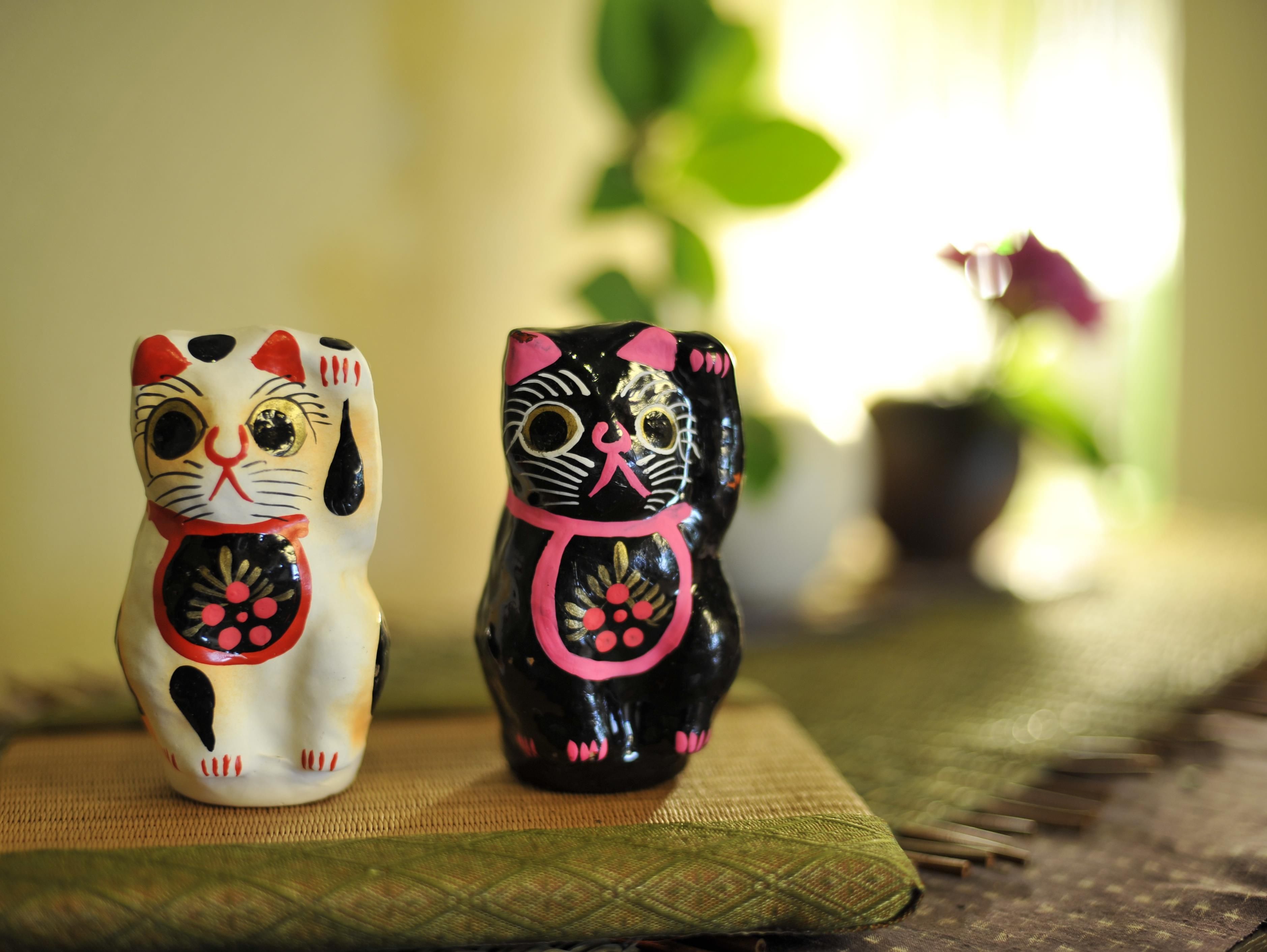 Two ceramic cat figurines on a woven mat.