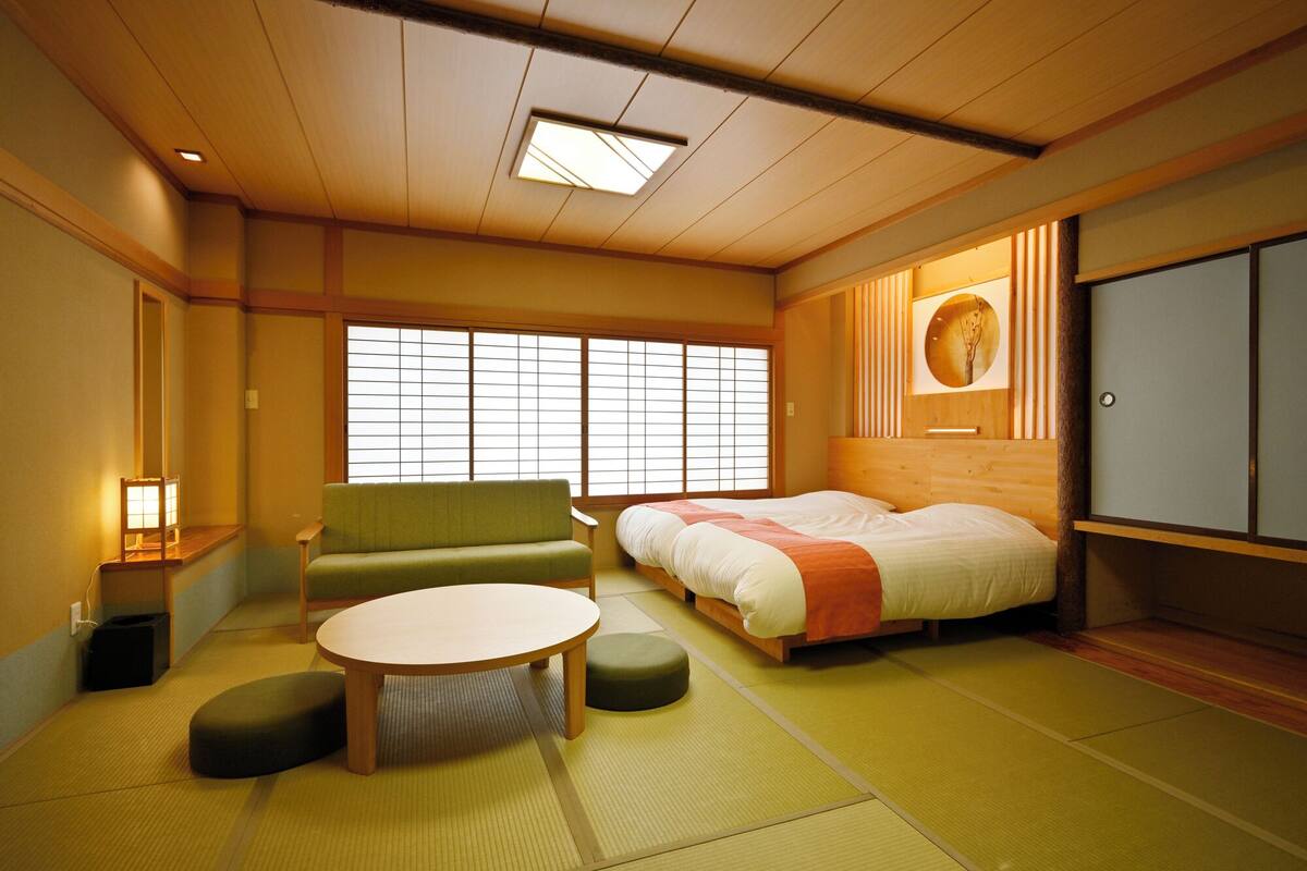 A traditional Japanese-style room with tatami flooring, a futon bed, a low table, and a shoji screen window.