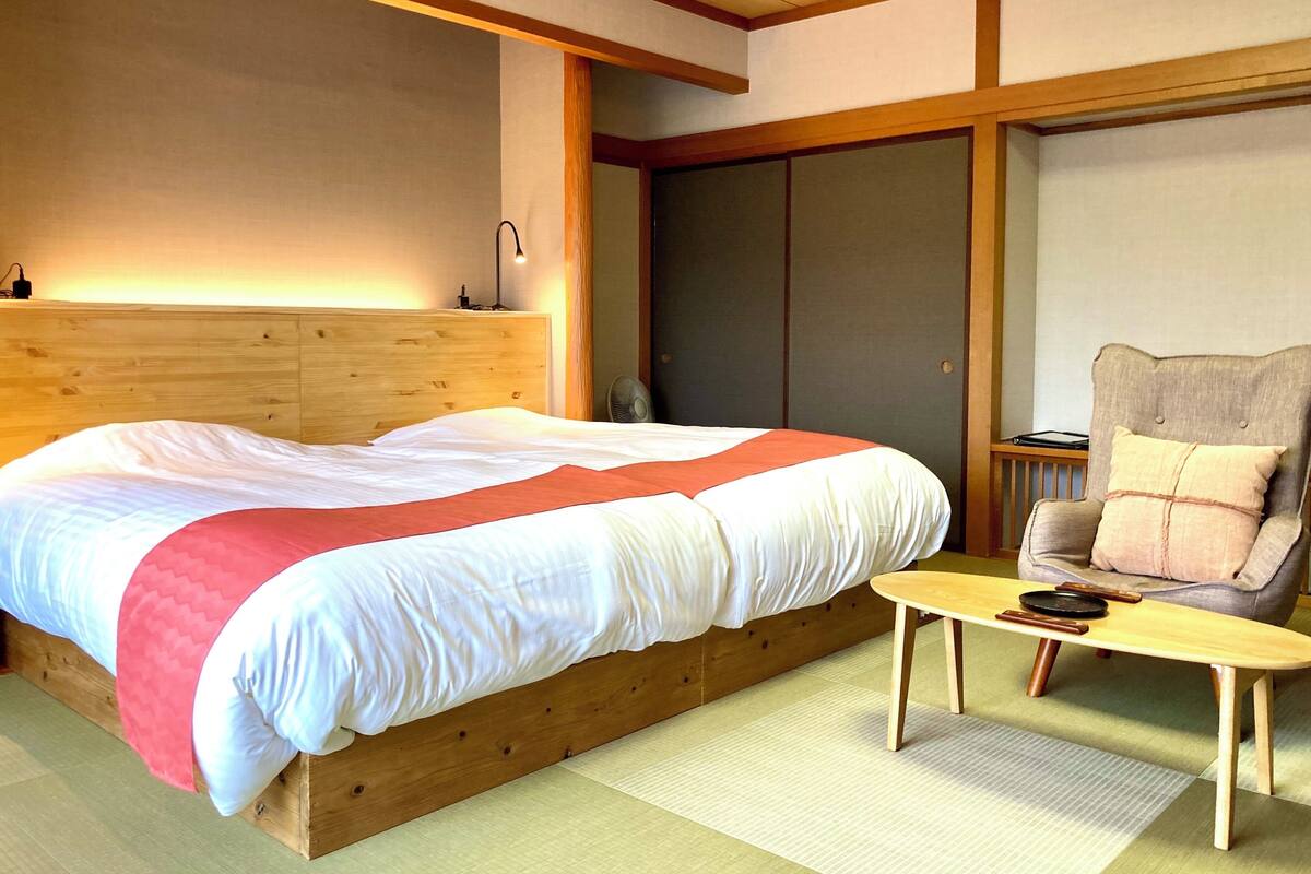 A bedroom with a wooden bed, a small table, a chair, and a sliding door.