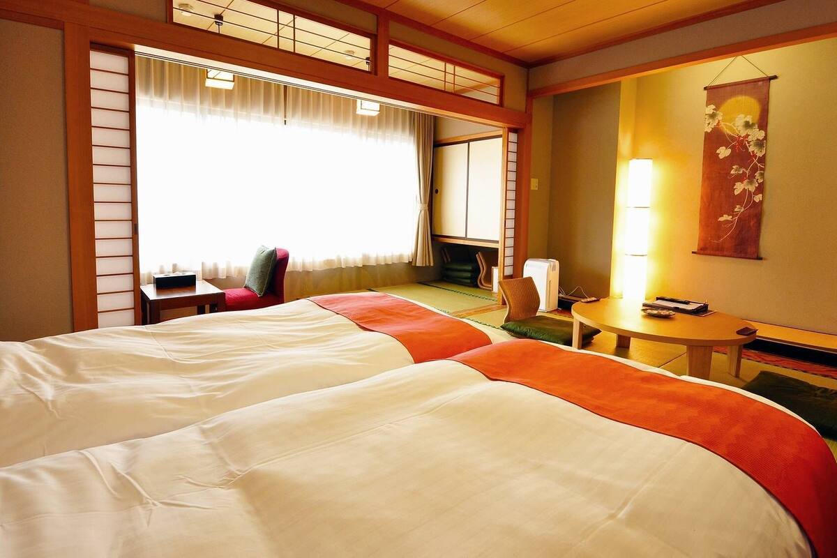 A hotel room with a large bed, a small table, a chair, and a desk with a lamp.
