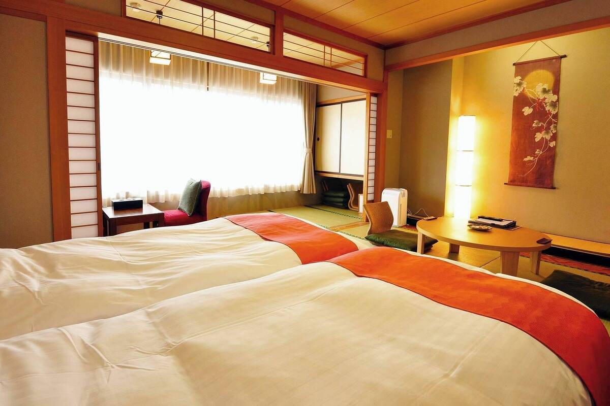 A hotel room with a large bed, a small table, a chair, and a view of the outside.