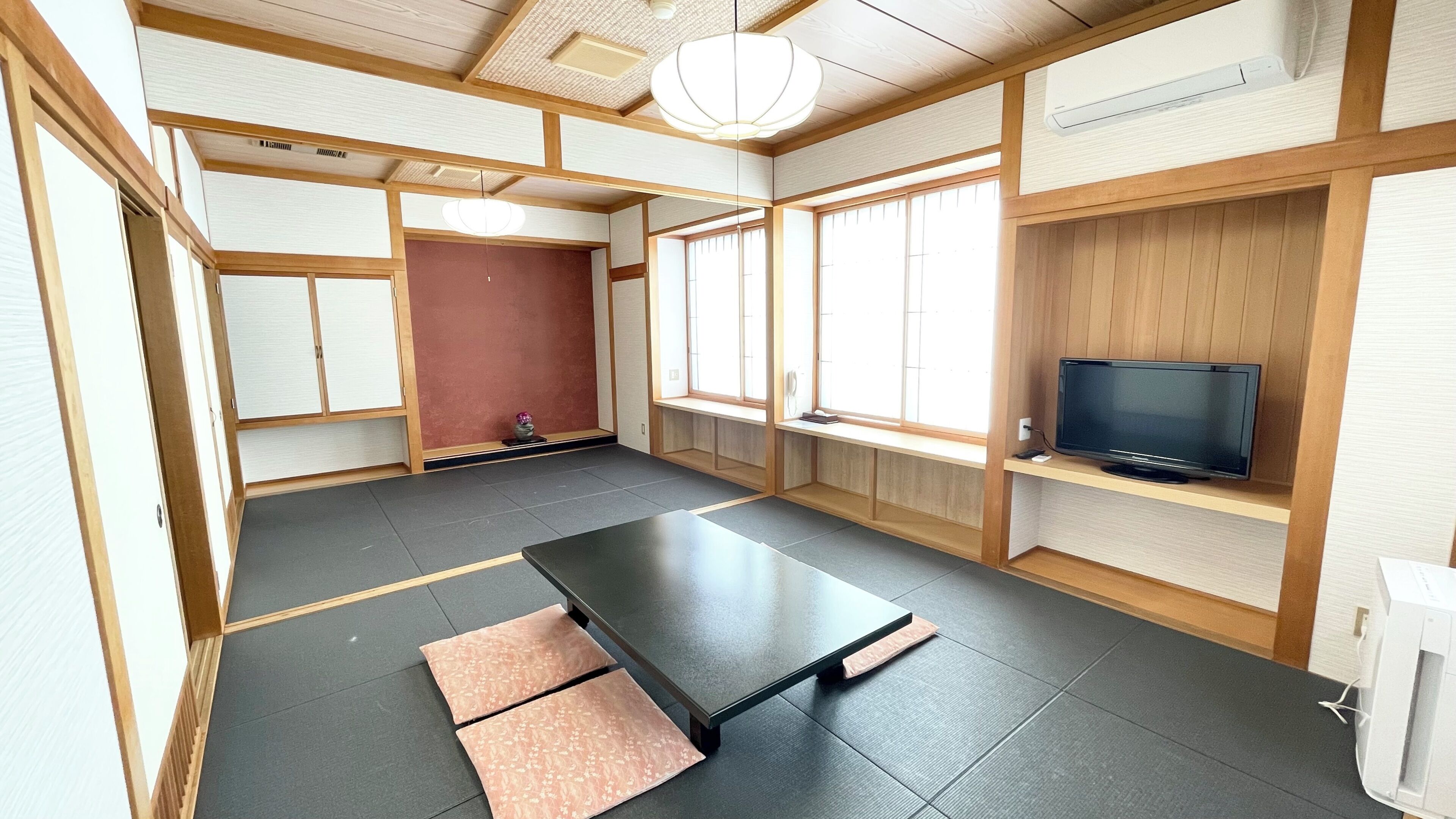 Une pièce de style japonais traditionnel, avec un sol recouvert de tatamis, une table basse, un téléviseur posé sur une étagère en bois et des portes coulissantes.