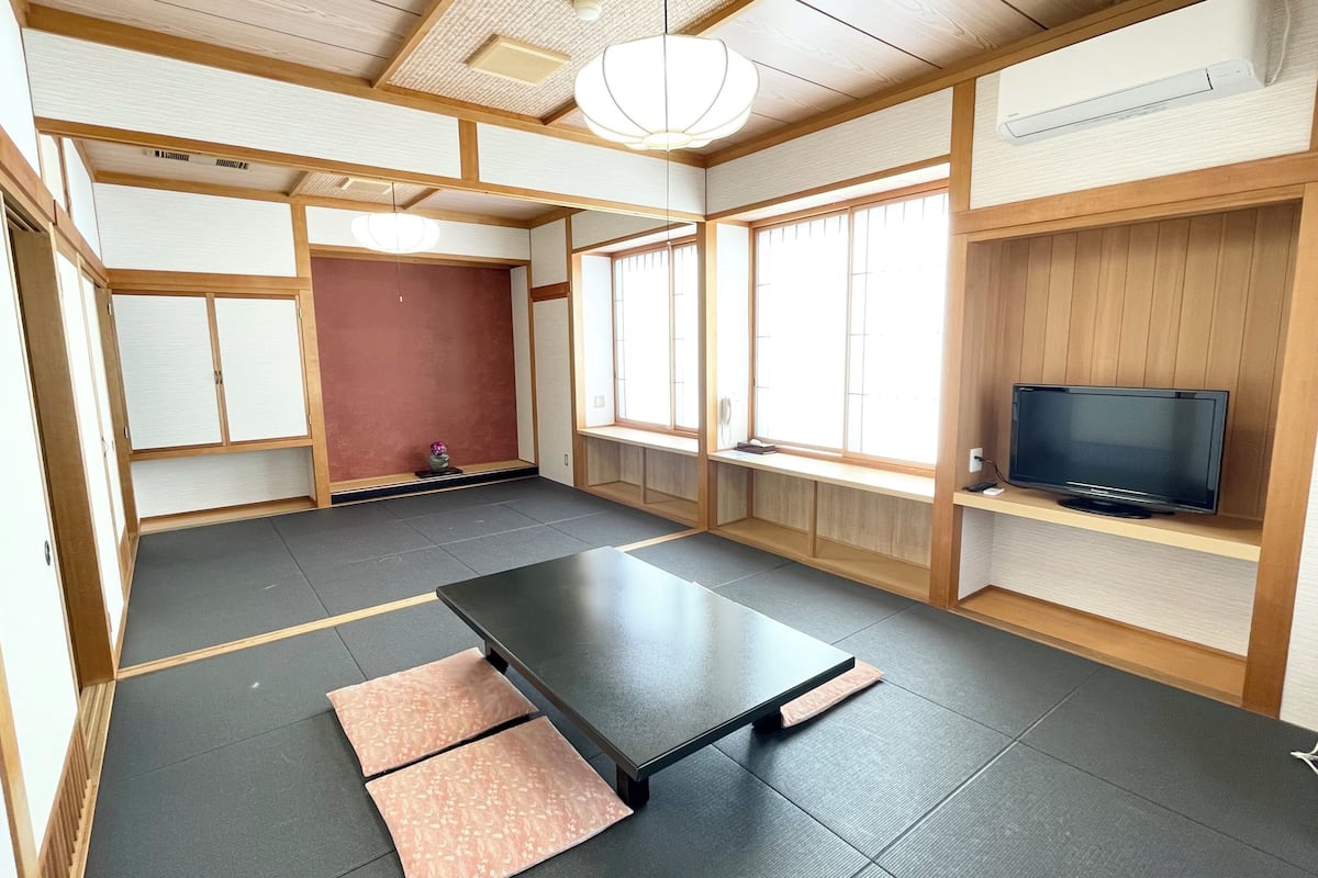 A traditional Japanese-style room with tatami flooring, a low table, a television on a wooden shelf, and sliding doors.