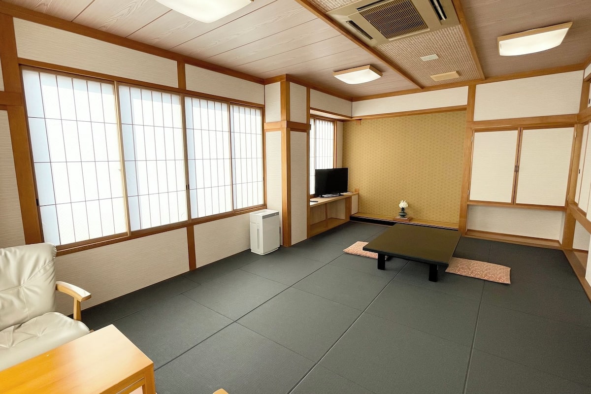 A traditional Japanese room with tatami flooring, shoji screens, a television, and a futon bed.