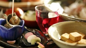 Una bandeja con diferentes alimentos, incluyendo un caracol, mochi y tofu.