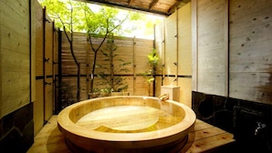 Una bañera de madera en una habitación con paredes de bambú y vistas a la vegetación exterior.