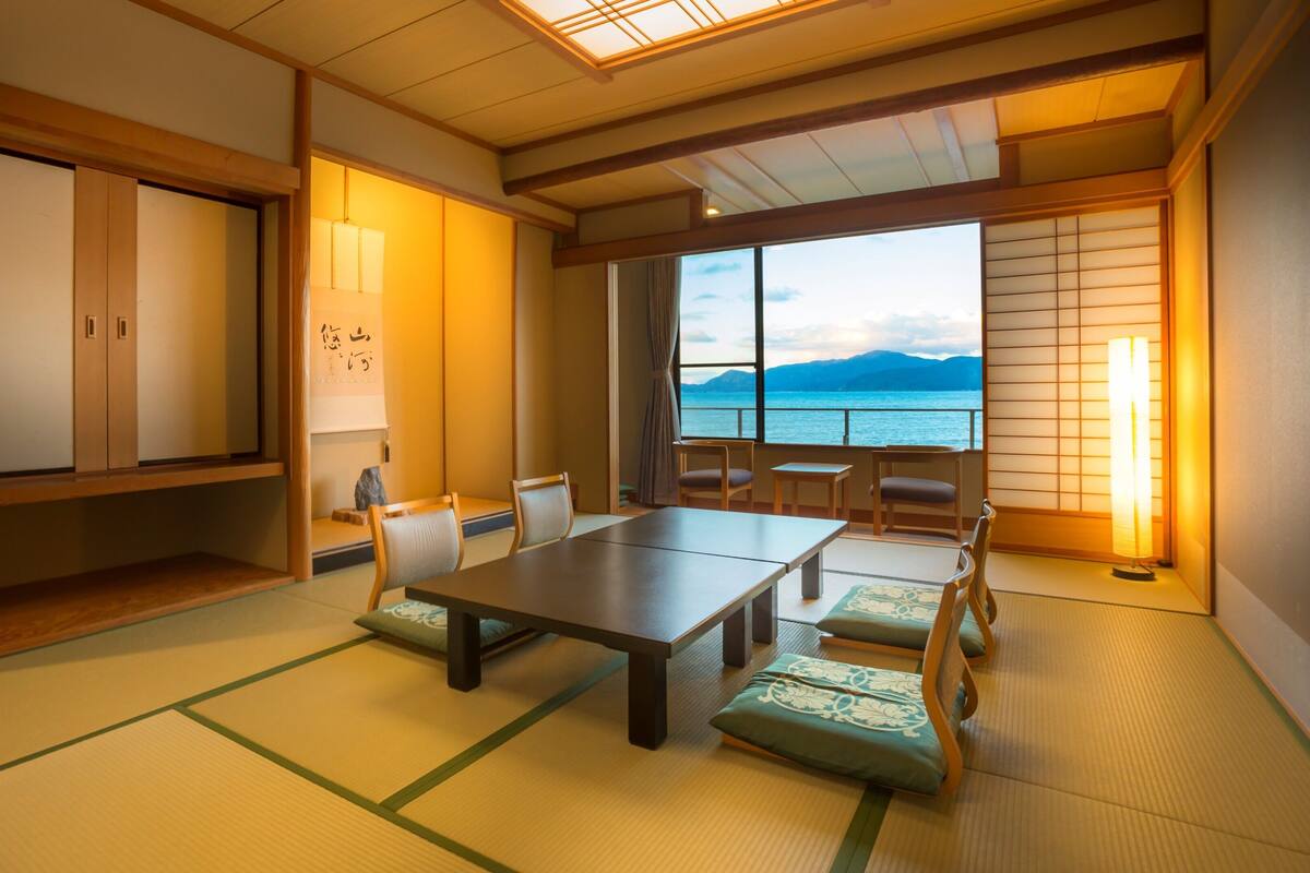 A traditional Japanese room with tatami flooring, a low table, and a view of the sea.
