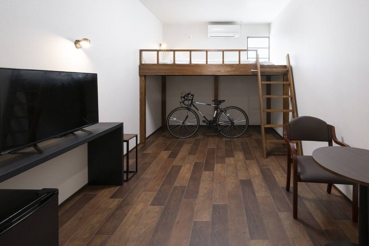 A compact room with a bunk bed, a bicycle, a TV, and a dining table.