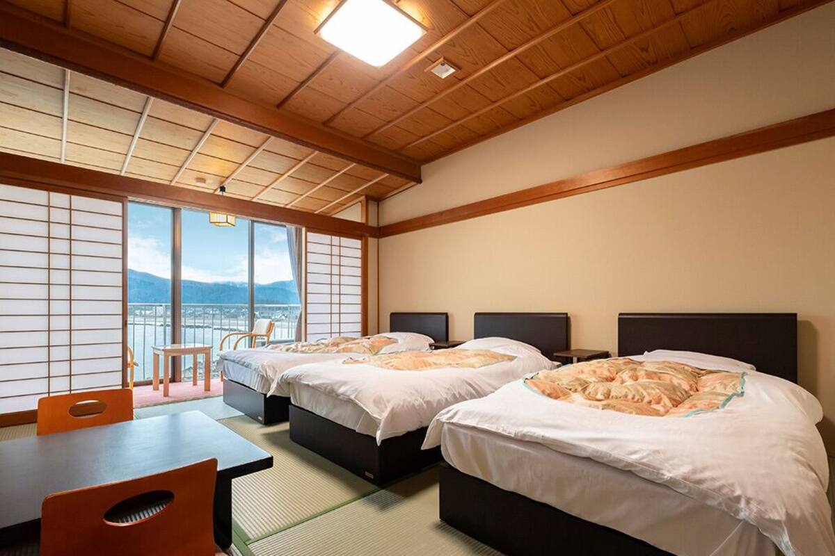 A hotel room with two beds, a table, and a view of mountains through large windows.