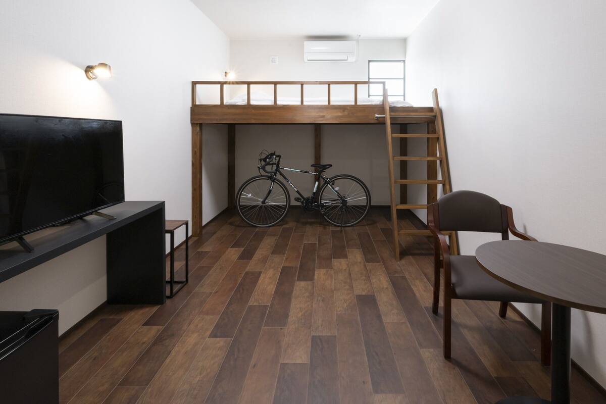 A compact room with a bunk bed, a bicycle, a TV, and a dining table.