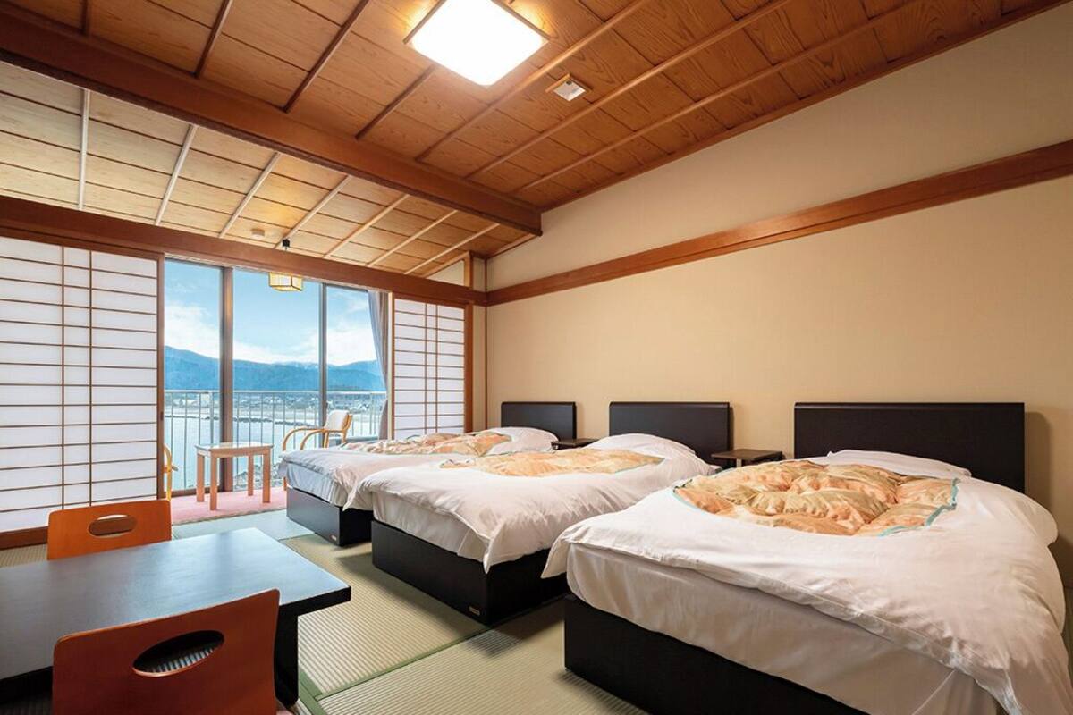 A hotel room with tatami flooring, two beds, a table, and a view of mountains.