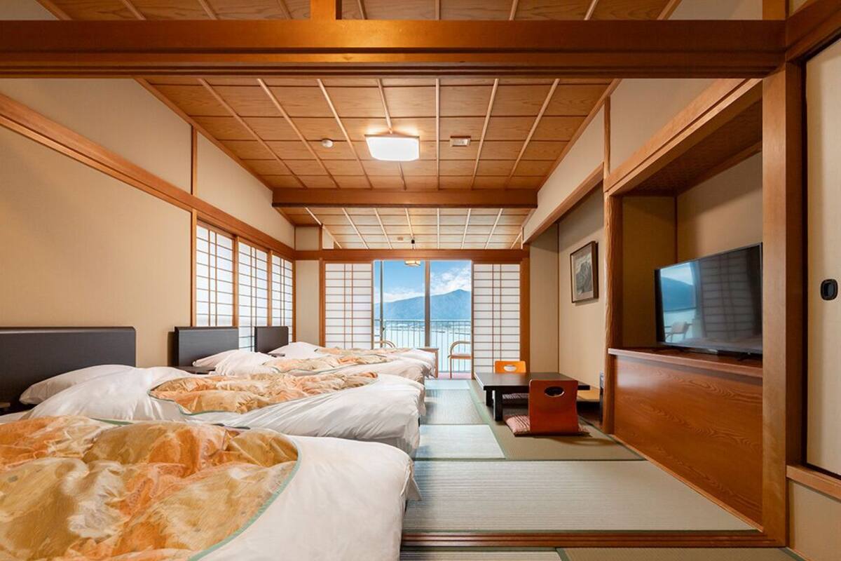 A hotel room with tatami mats, a TV, a desk, and a view of the mountains.
