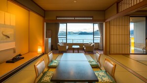Comedor con esteras de tatami, una mesa, sillas, un farol y vista al mar.