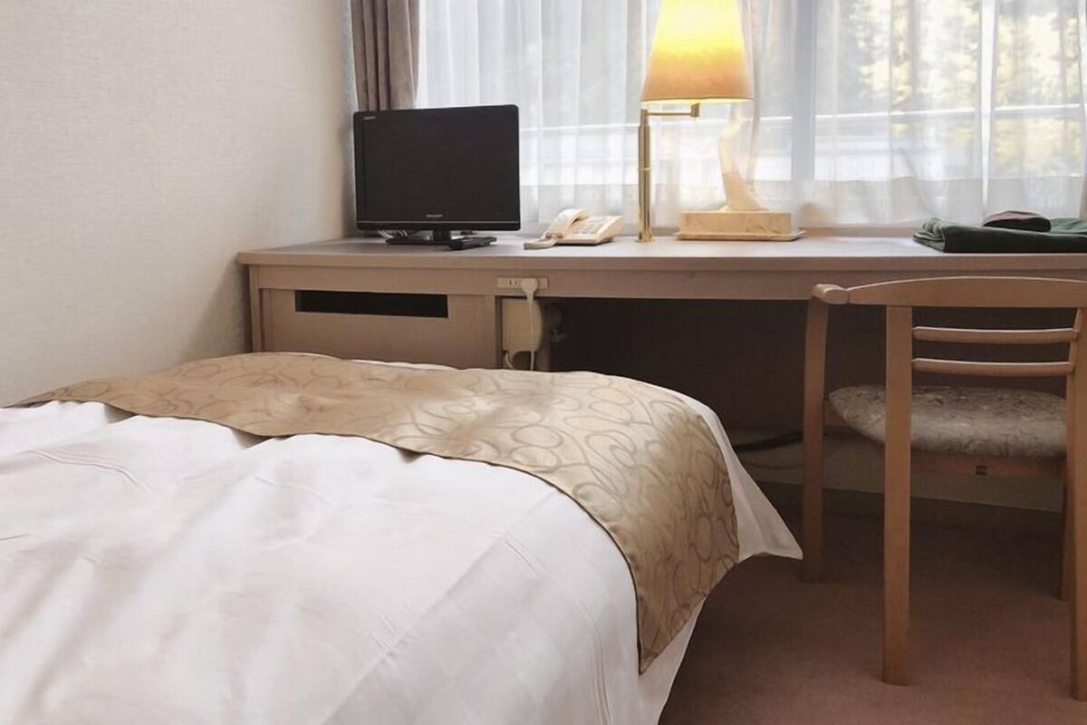 A hotel room with a bed, a desk with a computer, a lamp, and a chair.