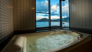 Un baño con bañera, una ventana con vistas al mar y a las montañas, y paredes de azulejos.