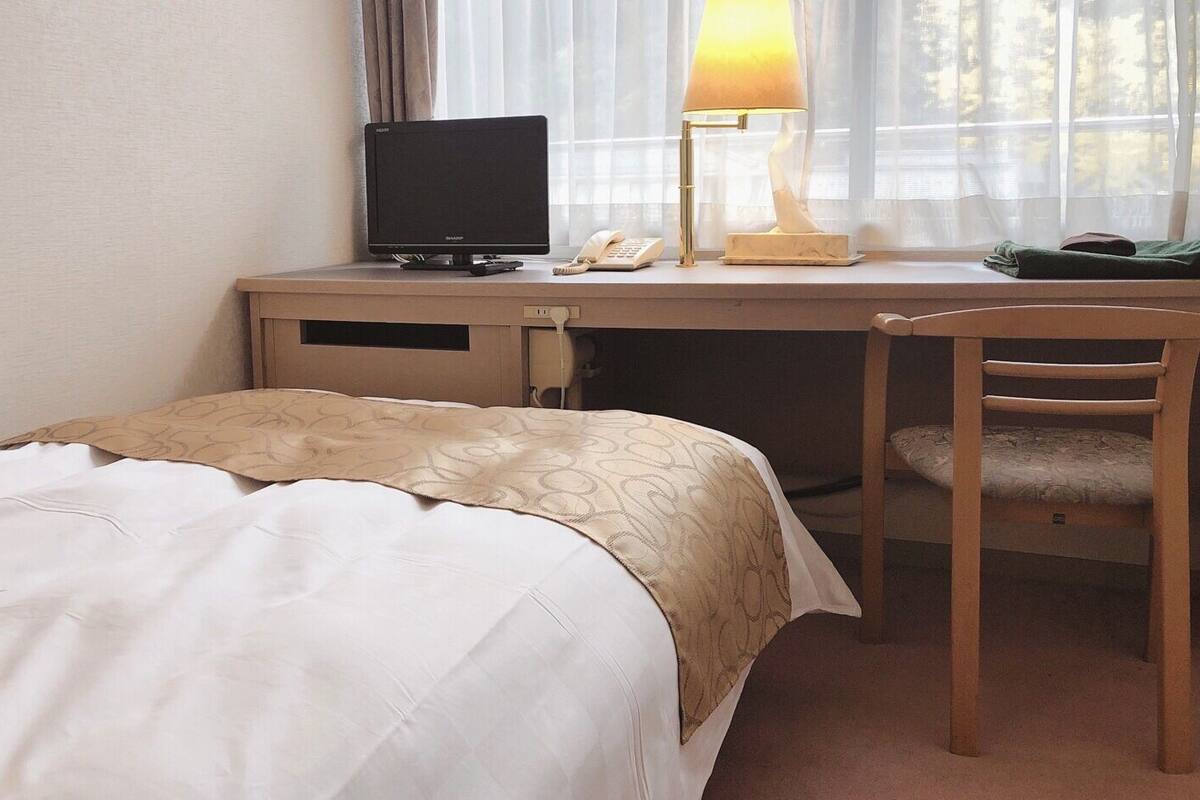 A hotel room with a bed, a desk with a computer, a lamp, and a chair.