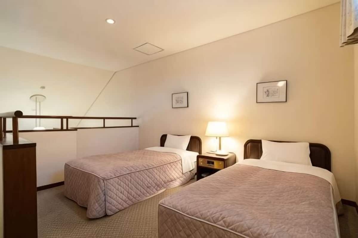 A hotel room with two beds, a desk, a chair, a lamp, and a small table.