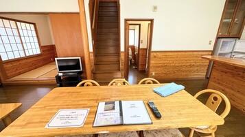 A traditional Japanese-style room with tatami flooring, a wooden dining table with chairs, a television, and a staircase leading to another level.