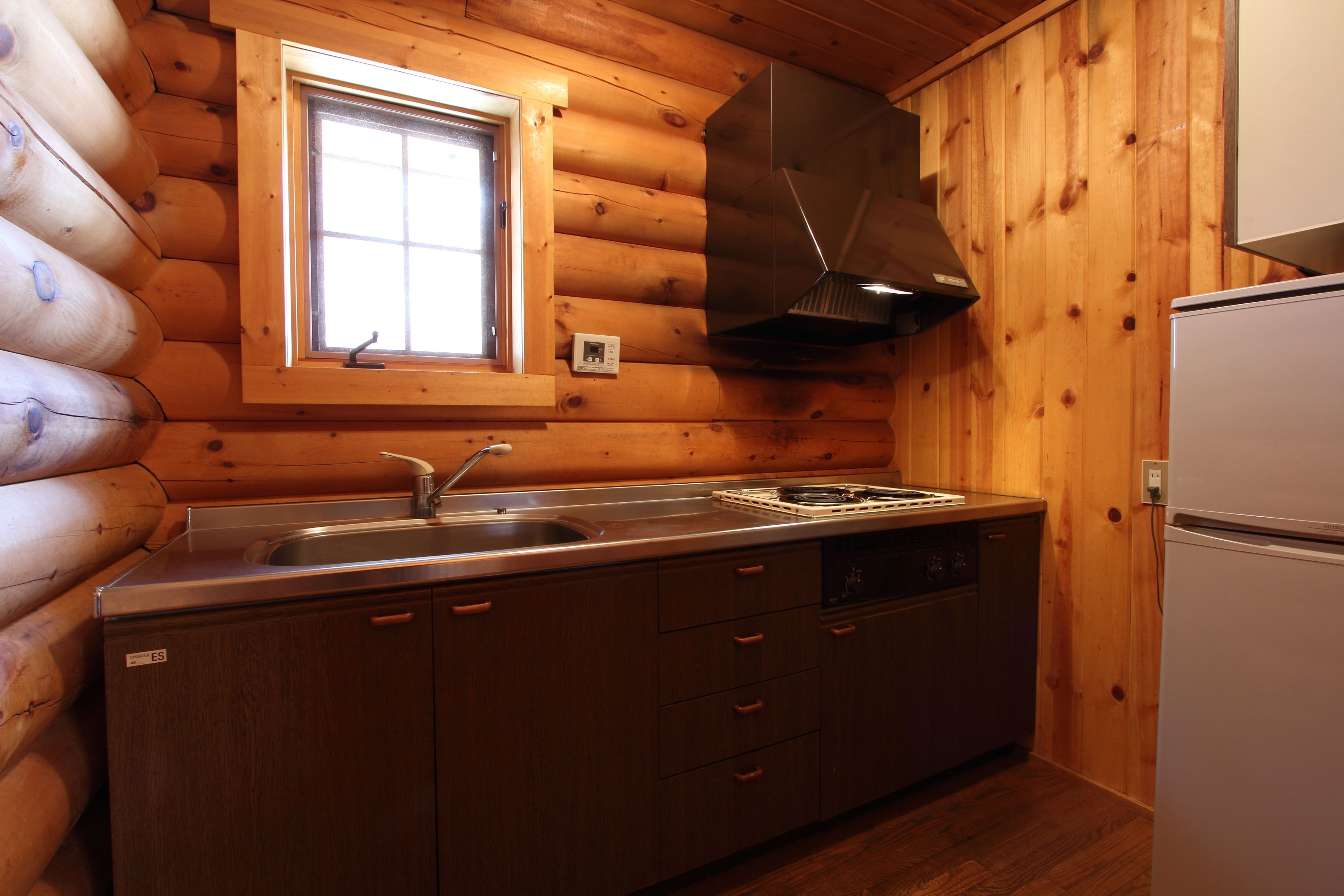 A log cabin kitchen with a built-in sink, stove, and a white refrigerator.